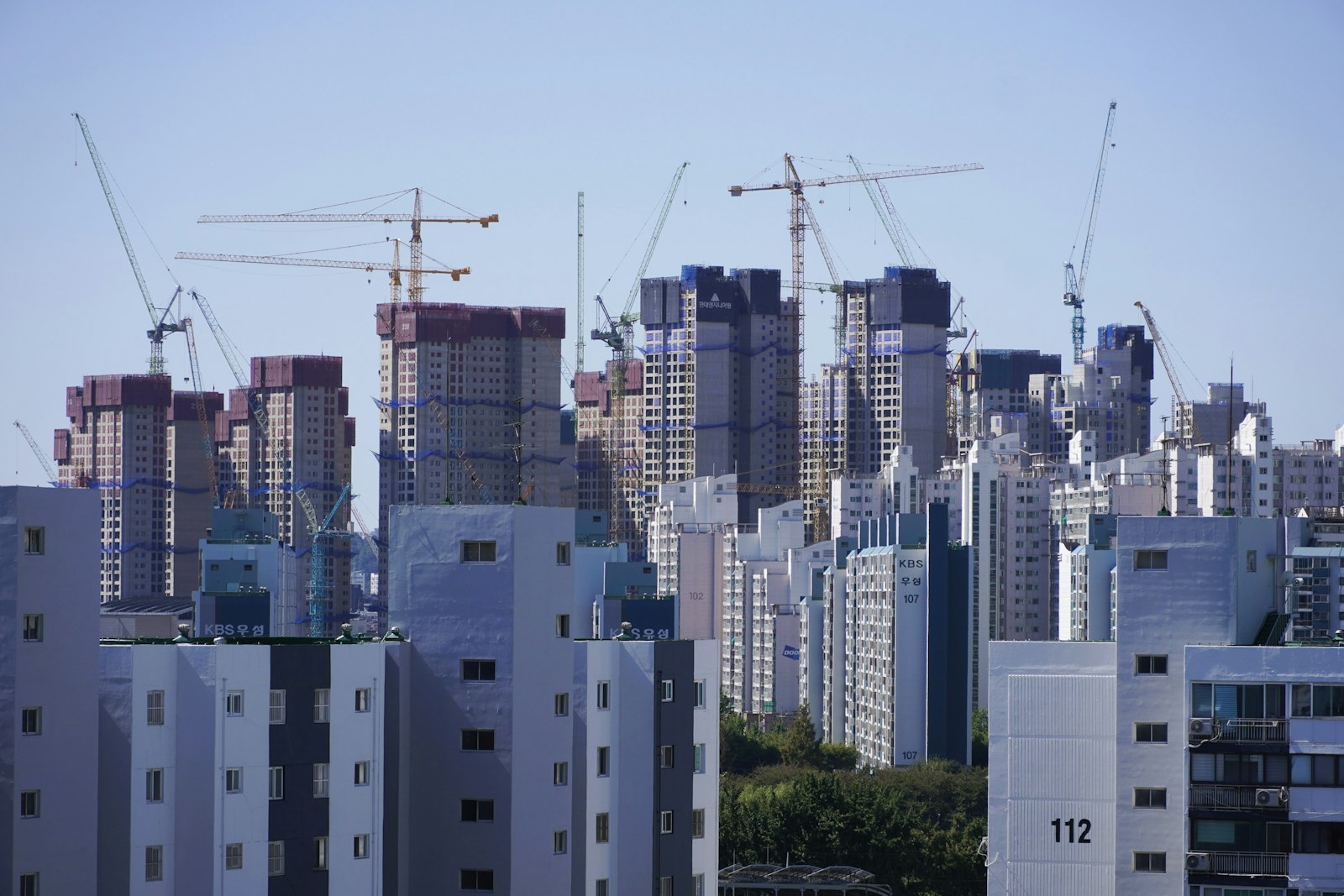 Rows of high-rise Korean apartment blocks, numbered building 112 in front, with construction cranes behind