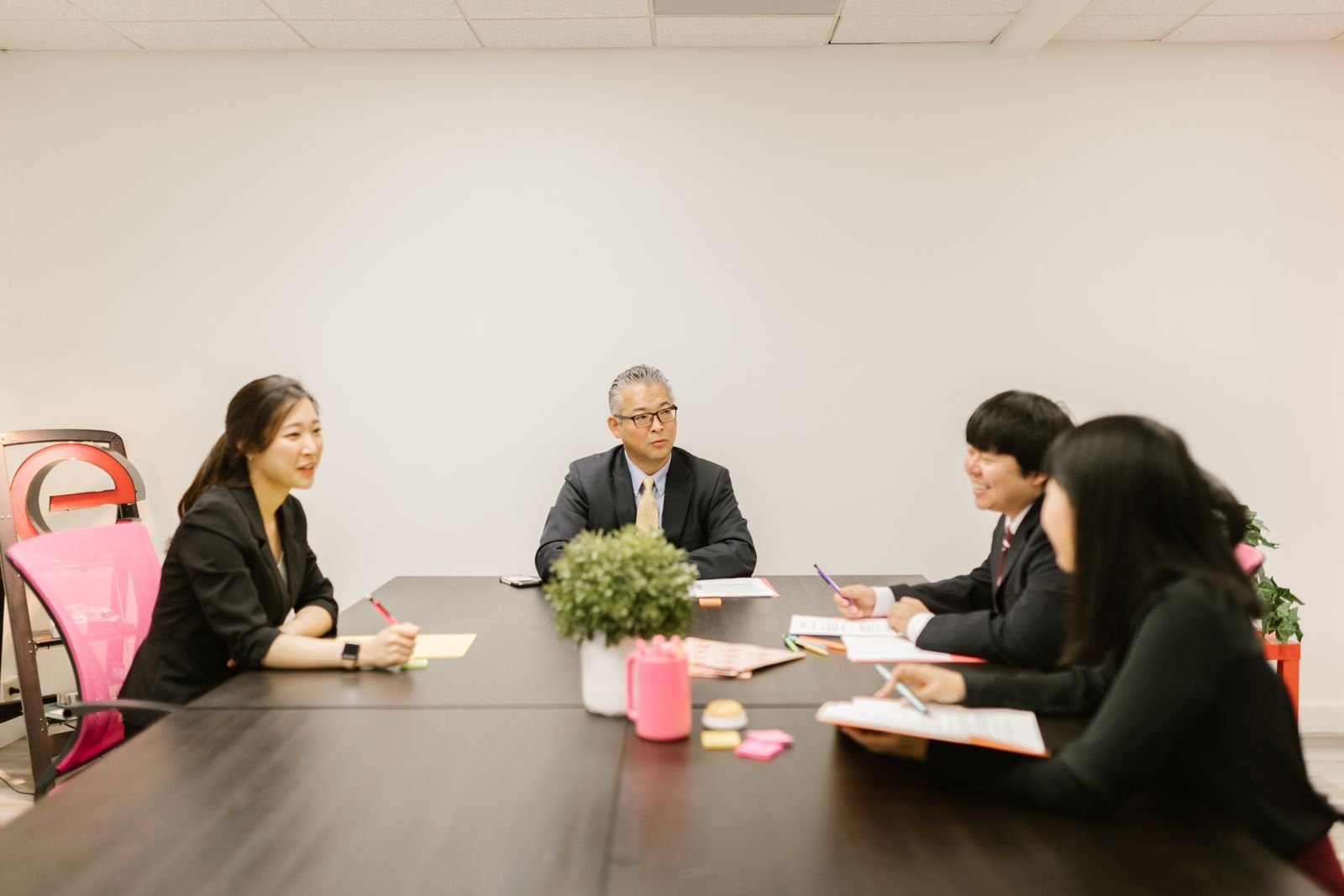A team meeting in an office, with a senior manager at the head of the table and junior staff along the sides